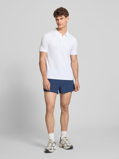 Männermodel trägt Slim Fit Poloshirt mit Logo Modell 'EDMOND' von Ellesse aus Material-Mix mit Stretch-Anteil in Weiß, Ganzkörperansicht von vorne.