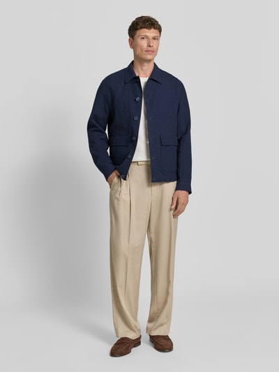 Męski model nosi Regular Fit Hemdjacke aus Leinen-Baumwoll-Mix od bugatti, miks lnu i bawełny, krój regular fit, kołnierzyk kent, zapięcie na guziki, kieszenie z patką, długość tyłu w rozmiarze 50: 67 cm, granatowa góra, beżowe spodnie, brązowe mokasyny, całopostaciowy widok z przodu.