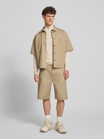 Męski model nosi Troyer mit Logo-Stitching und kurzem Reißverschluss von REVIEW, mieszanka bawełny, krój nowoczesny, kołnierz zapinany, prążkowane wykończenia, długość tyłu w rozmiarze M 65 cm, długość rękawów w rozmiarze M 66 cm, całkowity widok z przodu.