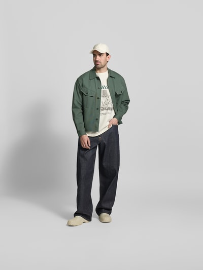 Männermodel trägt Regular Fit T-Shirt aus Baumwolle von RHUDE in Beige mit Label-Print und Foto-Print, Herren T-Shirt, Ganzkörperansicht von vorne. Rückenlänge bei Größe M: 72 cm, Rundhalsausschnitt, reine Baumwolle.
