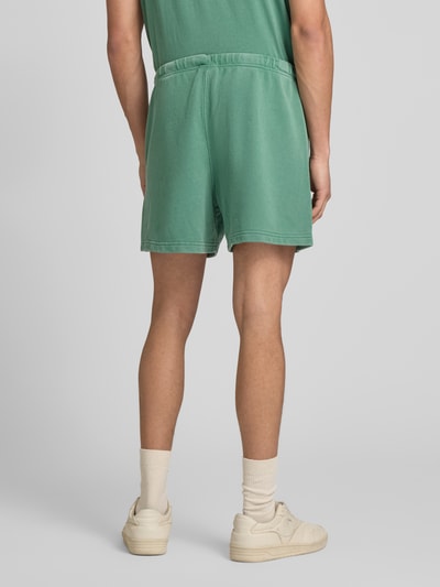 Männermodel trägt Sweatshorts mit Eingrifftaschen von CHAMPION in Grün, Baumwoll-Mix, Regular Fit, elastischer Bund, Ganzkörperansicht Rückansicht.