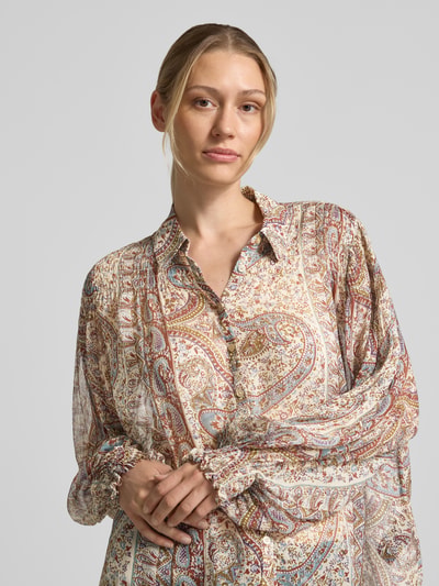Frauenmodel trägt Regular Fit Bluse aus reiner Viskose Modell 'Cleo' von ba&sh mit Allover-Paisley-Print, Umlegekragen, Smok-Detail, langärmelig, leichte Stoffstruktur in Beige- und Brauntönen, Nahaufnahme Oberkörper.