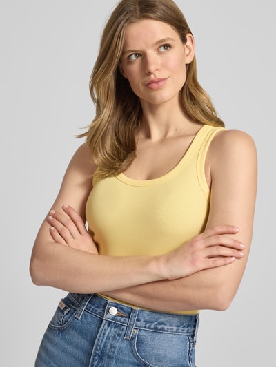 Kobiece model nosi top w kolorze żółtym, efekt prążkowania, mieszanka bawełny i elastanu, krój slim fit, model 'FRIDA' od JJXX, okrągły dekolt, długość tyłu w rozmiarze S: 54 cm, zdjęcie w formie zbliżenia na górną część ciała z przodu.