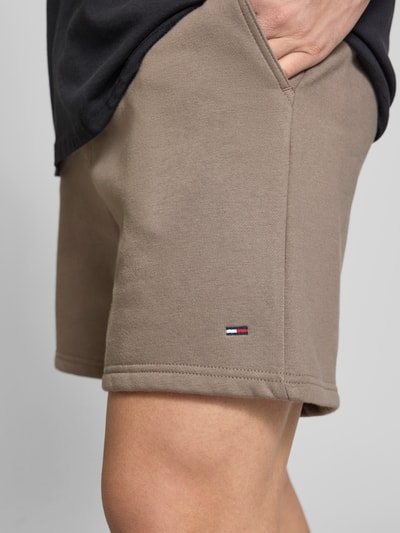 Männermodel trägt Regular Fit Shorts aus Baumwoll-Mix von Tommy Jeans in Beige mit Logo-Detail, Sweat-Textur, Nahaufnahme Oberschenkel.