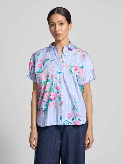 Kobiece model nosi Regular Fit Bluse aus Baumwolle im Allover-Look von Milano Italy, krój regular fit, kołnierzyk koszulowy, wzór na całej powierzchni, czysta bawełna, długość tyłu w rozmiarze 36: 62 cm, długość rękawów 4 cm, kolor niebieski z różowym i zielonym wzorem kwiatowym, widok całej sylwetki z przodu.