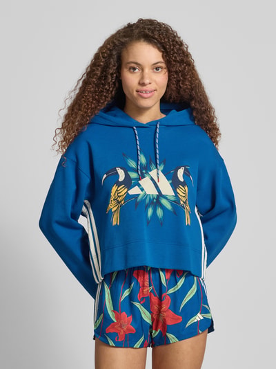 Kobiece model nosi Regular Fit Hoodie aus Baumwoll-Mix od adidas Sportswear, efekt: jednolity kolor, nadruk z motywem, kaptur z tunelem, długi rękaw, zakończenie rękawów i dołu prążkowane, dzianina dresowa, mieszanka bawełny, Ganzkörperansicht z przodu.