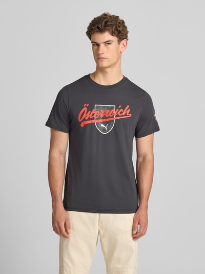 Männermodel trägt T-Shirt mit Print und Rundhalsausschnitt von PUMA PERFORMANCE in Schwarz, Reine Baumwolle, Regular-Fit, Ganzkörperansicht von vorne.