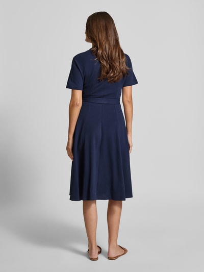 Frauenmodel trägt tailliertes Freizeitkleid aus reiner Baumwolle von Lacoste in unifarben Dunkelblau, Midi-Länge, Rückansicht.