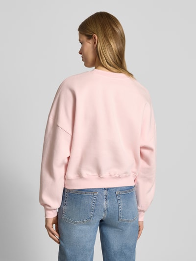Frauenmodel trägt Sweatshirt mit Label-Print und Rundhalsausschnitt von Review in Hellrosa aus Baumwoll-Mix, Relaxed-Fit, Ganzkörperansicht Rückansicht.