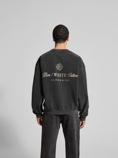 Männermodel trägt Oversized Sweatshirt aus Baumwoll-Mix von Don't Waste Culture, schwarz mit Statement-Print, Rückenlänge 67 cm, Ganzkörperansicht Rückansicht.