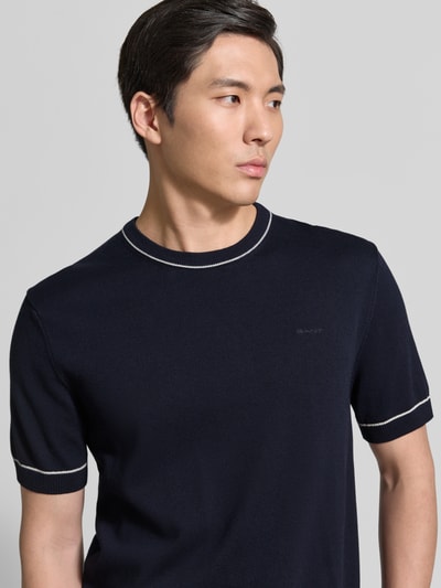 Männermodel trägt Strickshirt mit Rundhalsausschnitt von Gant in Dunkelblau, Baumwoll-Modal-Mix, kurze Ärmel, Nahaufnahme Oberkörper.