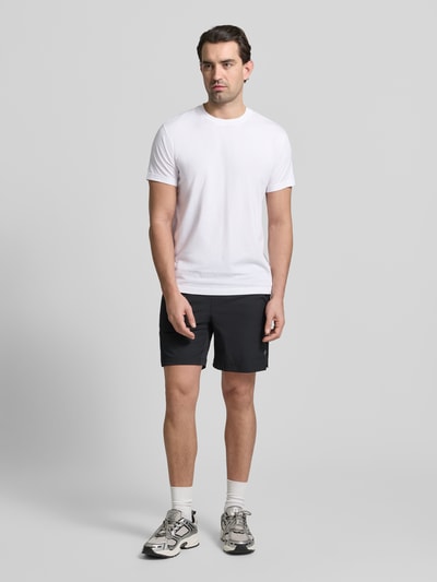 Męski model nosi Slim Fit T-Shirt mit Rundhalsausschnitt von Fabletics, bawełniana mieszanka z modalem, krój slim fit, krótkie rękawy, długość tyłu w rozmiarze M: 68 cm, biała góra, czarne szorty, neutralne kolory, gładka tekstura, całe ciało z przodu