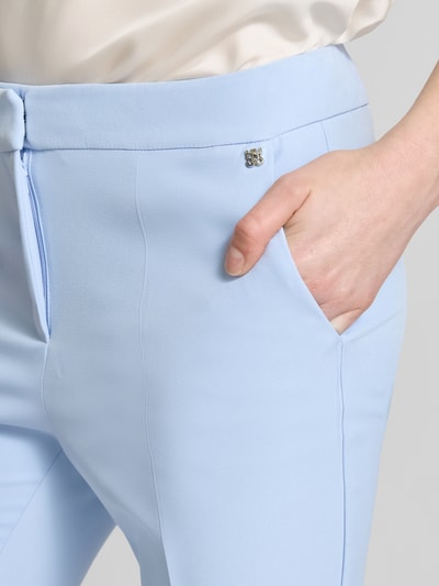 Frauenmodel trägt Slim Fit Hose mit Bügelfalten Modell 'HAGONIA-1' von HUGO in Hellblau, unifarben, mit Logo-Applikation und Eingrifftaschen, Nahaufnahme Oberkörper.