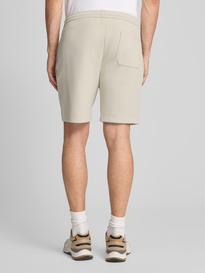 Männermodel trägt beigefarbene Shorts in glatter Optik, lockerer Schnitt, sichtbare Struktur, Ganzkörperansicht Rückansicht.