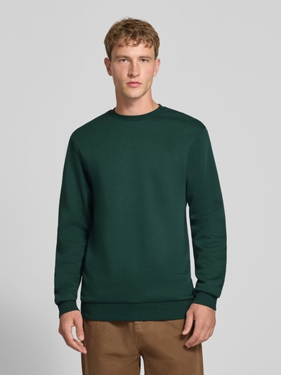 Männermodel trägt Regular Fit Sweatshirt aus Baumwoll-Mix Modell 'CERES' von ONLY & SONS in Dunkelgrün, glatte Struktur, Ganzkörperansicht von vorne.