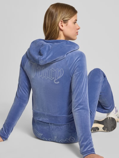 Frauenmodel trägt blaue Sweatjacke mit Kapuze Modell 'MADISON' von Juicy Couture aus Material-Mix mit Stretch-Anteil, Label-Detail, Ganzkörperansicht Rückansicht.