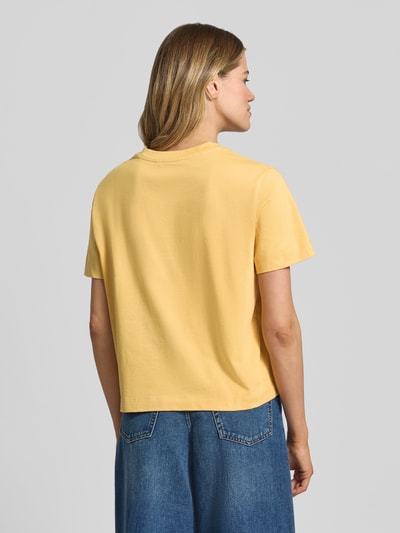 Modelka nosi Boxy Fit T-Shirt aus reiner Baumwolle Modell 'ESSENTIAL' von Selected Femme, jednokolorowe, heavy jersey, luźny krój, naszywka z logo, żółty, okrągły dekolt, krótki rękaw, widok całej sylwetki od tyłu.