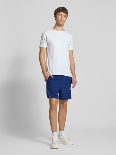 Männermodel trägt Regular Fit Sport-Shorts mit elastischem Bund von adidas Sportswear, unifarben blau, Kontraststreifen, Ganzkörperansicht von vorne.