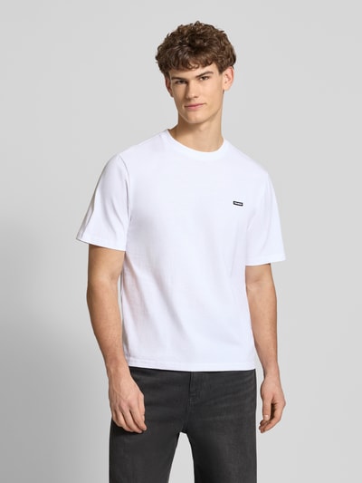 Männermodel trägt Basic T-Shirt mit kleinem Logo-Patch auf der Brust von REVIEW in Weiß, reine Baumwolle, gerader Schnitt, Nahaufnahme Oberkörper.