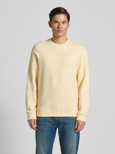 Männermodel trägt Sweatshirt mit Logo und Rundhalsausschnitt von Guess in Gelb, reine Baumwolle, Regular Fit, Ganzkörperansicht von vorne.