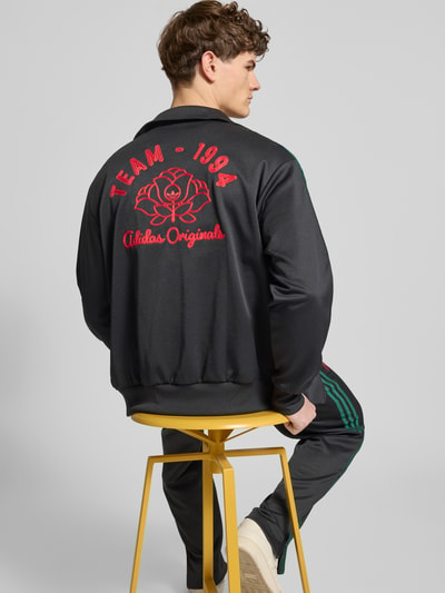 Männermodel trägt Sweatjacke mit Logo-Stitching und Stehkragen van adidas Originals, zwart met rode accenten, katoenmix, rechte fit, elastische boorden, rits, zijzakken, rugdetail, Ganzkörperansicht Rückansicht.