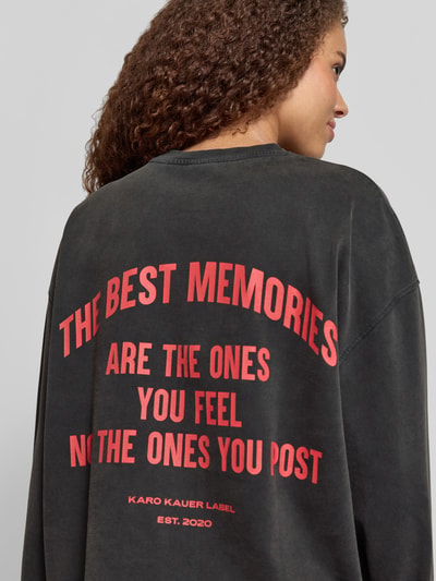 Frauenmodel trägt Oversized Longsleeve mit Logo-Print Modell 'Memories' von Karo Kauer in Schwarz mit rotem Print, Reine Baumwolle, Oversized-Fit, Rundhalsausschnitt, Rückenlänge bei Größe S: 63 cm, Ganzkörperansicht Rückansicht.