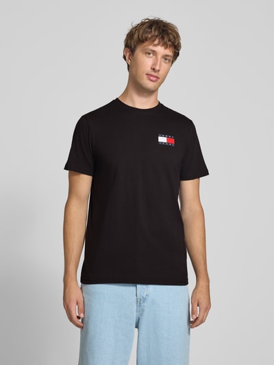 Männermodel trägt schwarzes Slim Fit T-Shirt aus reiner Baumwolle von Tommy Jeans, dezentes Logo vorn, Ganzkörperansicht von vorne. Herren T-Shirt von Tommy Jeans