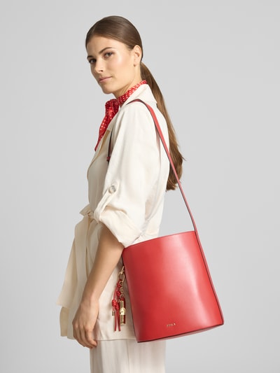 Männermodel trägt Bucket Bag mit Logo-Applikation Modell 'Roxie' von FURLA in Rot, glatte Textur, Hauptfach mit Magnetverschluss, Reißverschlussfach innen, verstellbarer Schulterriemen, Szerokość w rozmiarze 1: 24 cm, długość 26 cm, głębokość 17 cm, długość paska 67 cm, Ganzkörperansicht von vorne.