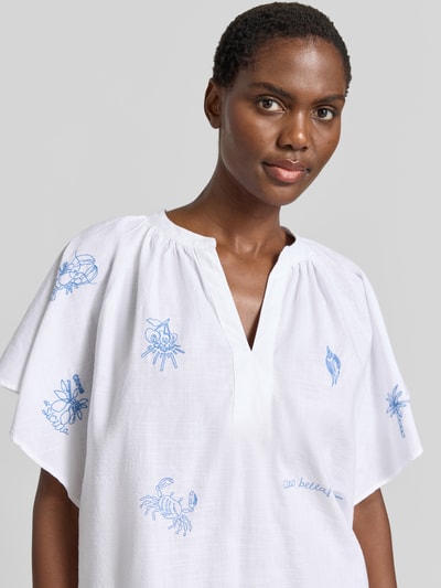 Frauenmodel trägt Relaxed Fit Tunikabluse mit Stitchings von Oui aus reiner Baumwolle, weiß mit blauen Stickereien, Nahaufnahme Oberkörper.