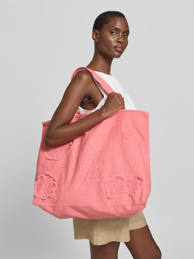 Frauenmodel trägt Strandtasche aus Baumwolle Modell 'Dieuw' von Barts in Rosa mit Stickdetails, Hauptfach mit Schnürung, Nahaufnahme Oberkörper. Breite 53 cm, Länge 39 cm, Tiefe 19 cm, Schulterriemen 52 cm, Innenfach mit Reißverschluss, Tragehenkel.