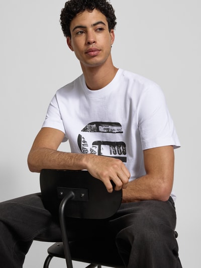 Männermodel trägt Regular Fit T-Shirt mit Logo-Print Modell 'icon' von G-Star Raw aus reiner Baumwolle, Weiß mit schwarzem Print, Nahaufnahme Oberkörper.