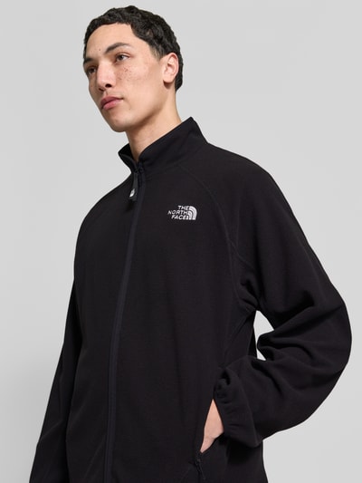 Männermodel trägt Fleecejacke mit Label-Stitching von The North Face in zwart, regular fit, met opstaande kraag, rits, detailopname bovenlichaam.