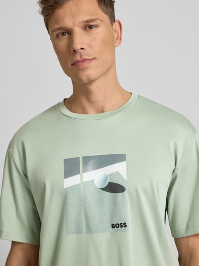 Männermodel trägt Relaxed Fit T-Shirt aus reiner Baumwolle Modell 'JOIN' von BOSS Green in Hellgrün mit Motiv-Print, Nahaufnahme Oberkörper.