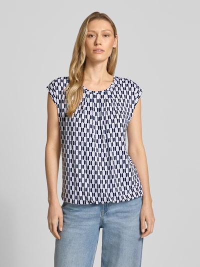 Vrouwenmodel draagt Blusenshirt mit Rundhalsausschnitt van ZABAIONE in mix van viscose en elastaan, recht model, korte mouwen, ruglengte maat S 58 cm, geometrisch patroon in blauw en wit, ronde hals, zachte gladde textuur, vooraanzicht bovenlichaam.