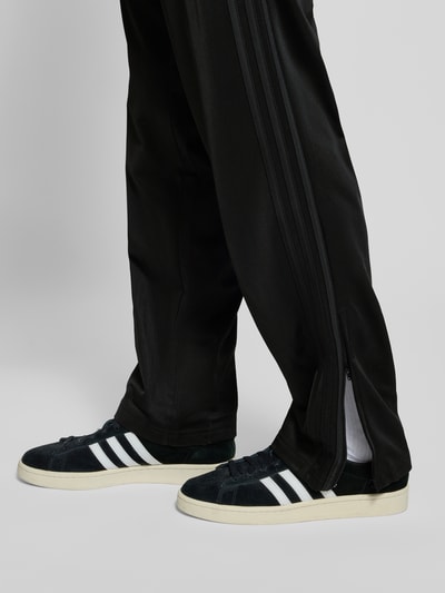 Männermodel trägt schwarze Trainingshose mit elastischem Bund, Reißverschlusstaschen, FIREBIRD von adidas Originals, Nahaufnahme Beine.