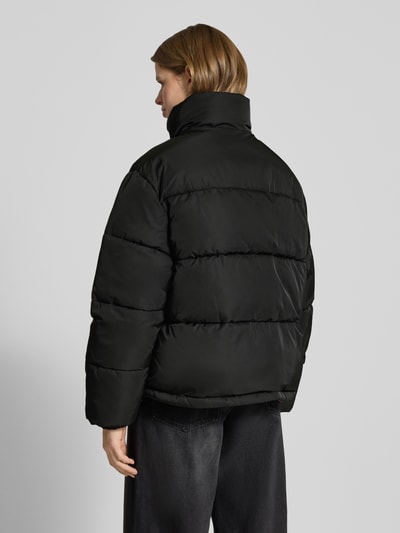 Modelka kobieca nosi 'Jacke mit Logo-Print' od Calvin Klein Jeans, czarny kolor, prosty krój, matowa tekstura, widok sylwetki od tyłu, kontekst: damska kurtka, unikatowy design, stójka, logo print, elastyczne mankiety, długość tyłu w rozmiarze M: 66 cm, szerokość ramion w rozmiarze M: 63 cm, szerokość klatki piersiowej w rozmiarze M: 60 cm, długość rękawa w rozmiarze M: 63 cm