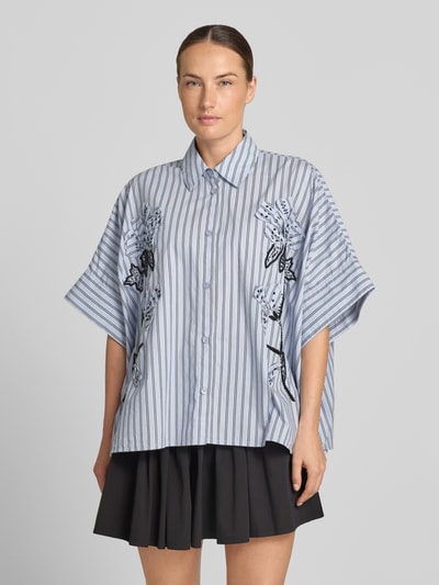 Frauenmodel trägt Oversized Kurzarmbluse aus reiner Baumwolle Modell 'JONKOE' von Essentiel Antwerp, feine blaue Streifen, Stickdetails, lockere Passform, Ganzkörperansicht von vorne. Damen Kurzarmbluse von Essentiel Antwerp.