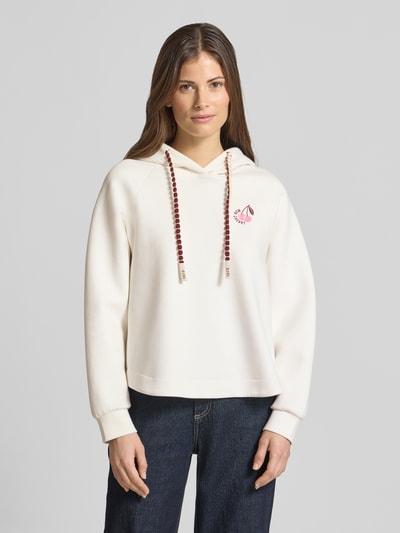 Kobiece modelka nosi Relaxed Fit Hoodie mit Motiv-Print von Marc Cain z mieszanki bawełny, krój relaxed fit, nadruk z motywem i napisem, kaptur z tunelem, elastyczne zakończenia rękawów, widok całej sylwetki od przodu.