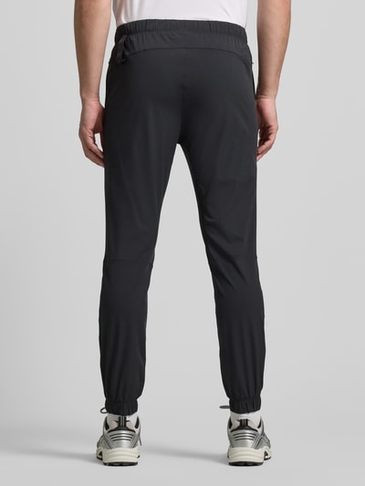 Männermodel trägt Slim Fit Sweatpants mit Logo-Print von Fabletics in Schwarz, elastischer Bund, Reißverschlusstaschen, Rückansicht Ganzkörperansicht.