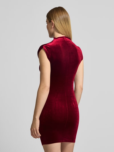 Frauenmodel trägt Cocktailkleid mit seitlicher Raffung von APRICOT, unifarbenes Samtmaterial in Rot, Mini-Länge, hochgeschlossen, ohne Ärmel, Ganzkörperansicht Rückansicht.