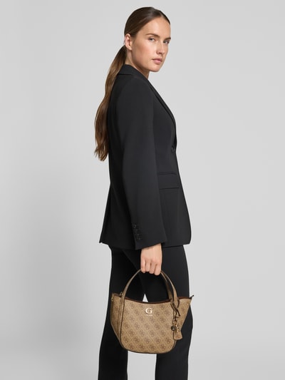 Frauenmodel trägt Handtasche in Leder-Optik Modell 'Coleen' von Guess mit Allover-Logo-Print, Magnetverschluss, Nahaufnahme Oberkörper.