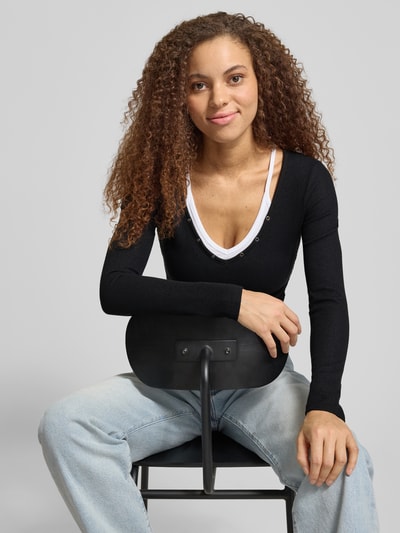 Frauenmodel trägt Slim Fit Longsleeve mit Strukturmuster von Guess Jeans im Layered-Look, Elastischer-Material-Mix, Nahaufnahme Oberkörper.