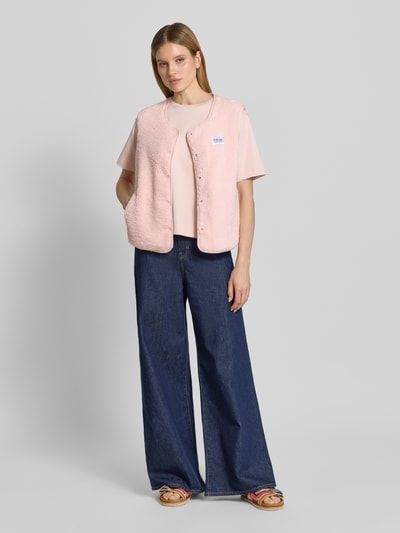 Frauenmodel trägt Regular Fit Weste in Teddy-Optik Modell 'AMALIA' von VILLA SOPHIE in zartem Rosa mit Label-Patch, seitlichen Eingrifftaschen, Druckknopfleiste, Materialverarbeitung aus Teddyfell, Ganzkörperansicht von vorne.