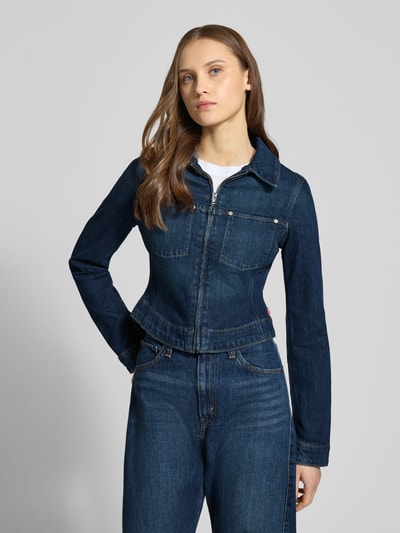 Modelka kobieca nosi Jeansjacke mit Reißverschluss und Label-Detail od Levi's®, granatowy dżins, krój slim fit, bawełna z elastanem, widoczny kołnierz, srebrny zamek błyskawiczny, detal z logo, długość tyłu w rozmiarze S: 43 cm, szerokość ramion w rozmiarze S: 38 cm, szerokość klatki piersiowej w rozmiarze S: 45 cm, długość rękawa w rozmiarze S: 64 cm, widok całej sylwetki od przodu