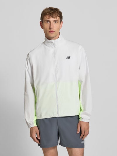Männermodel trägt Regular Fit Jacke in Stehkragen Modell 'Fast Days' von New Balance, Logo-Print, Reißverschluss, Eingrifftaschen, Elastische Ärmelabschlüsse, Tunnelzug im Bund, weiß mit gelbem Farbverlauf, glatte Textur, Ganzkörperansicht von vorne.