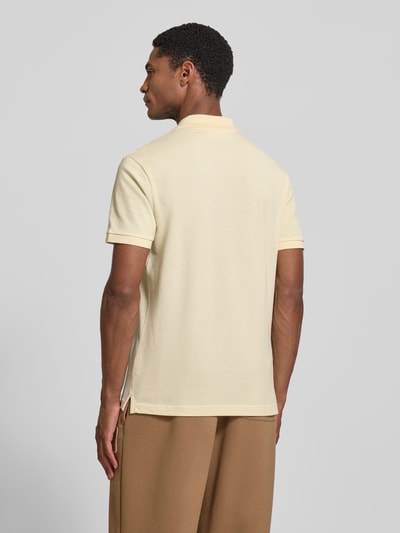 Männermodel trägt Slim Fit Poloshirt aus reiner Baumwolle von Lacoste in Beige, dezente Struktur, glatte Oberfläche, Ganzkörperansicht Rückansicht.