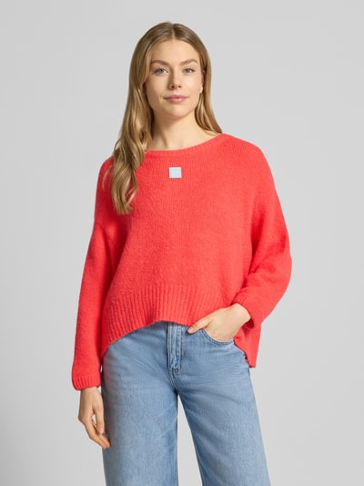 Frauenmodel trägt Relaxed Fit Pullover mit Alpaka-Anteil Modell 'East' von American Vintage in Strick-Optik, Statement-Detail, U-Boot-Ausschnitt, Elastischer-Material-Mix, elastische Abschlüsse, leuchtendes Rot, Rückenlänge 42 cm, Ärmellänge 42 cm, Ganzkörperansicht von vorne.