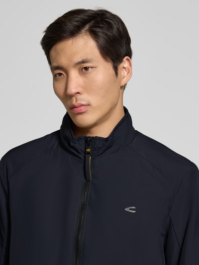 Männermodel trägt Blouson mit Logo-Print und Stehkragen von camel active in Dunkelblau, Reißverschluss, Label-Patch, Nahaufnahme Oberkörper.