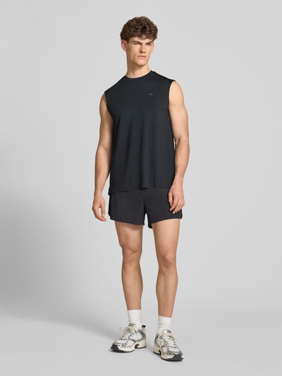 Männermodel trägt Relaxed Fit Top mit Logo-Print Modell 'OLIOS' von Ellesse aus Elastischer-Material-Mix, schwarz, Rundhalsausschnitt, Ganzkörperansicht von vorne. Rückenlänge bei Größe M: 74 cm.