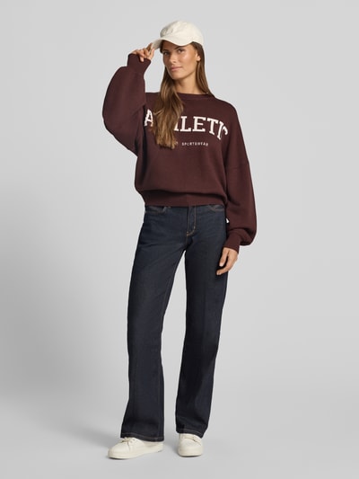 Frauenmodel trägt Oversized Strickpullover aus Viskose-Mix von aim'n, dunkles Braun, Label-Stitching, lockere Passform, Ganzkörperansicht von vorne.